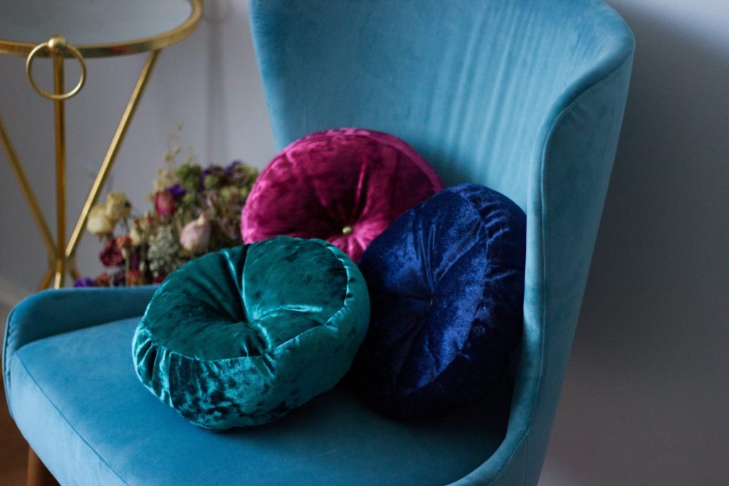 three round blue, teal, and pink velvet throw pillows on teal fabric swan chair