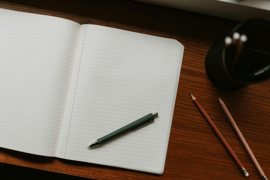 Open notebook with pen and pencils on desk